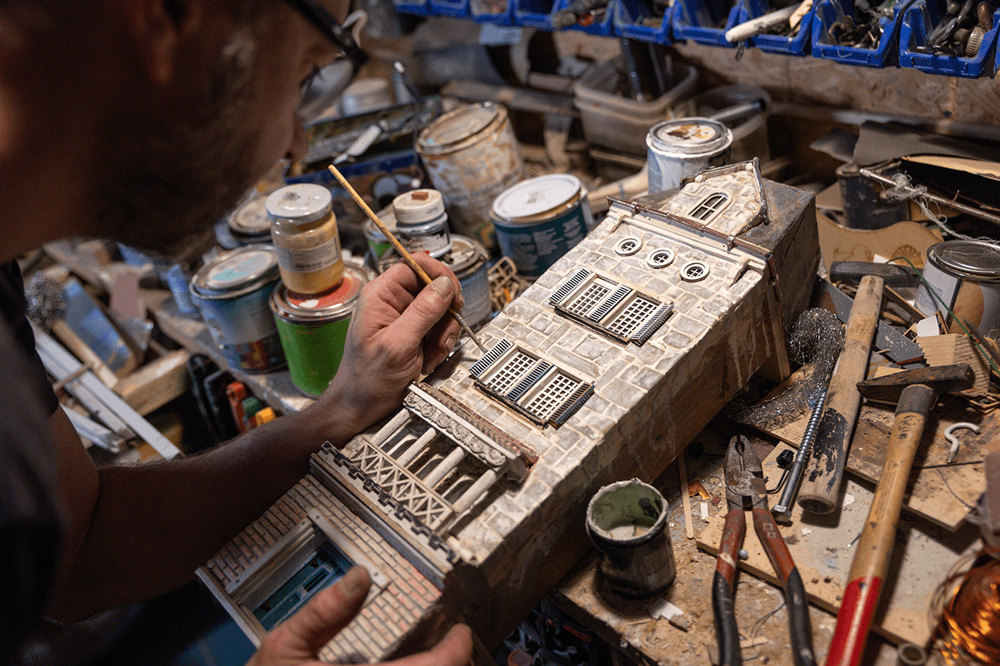 Model maker painting a miniature building at a workbench with tools
