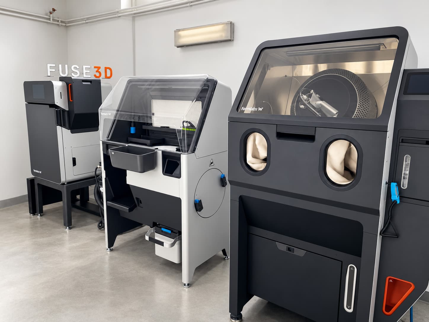 Fuse Blast with its working gloves and drum chamber, next to Fuse Sift and a Fuse printer at fuse3d.