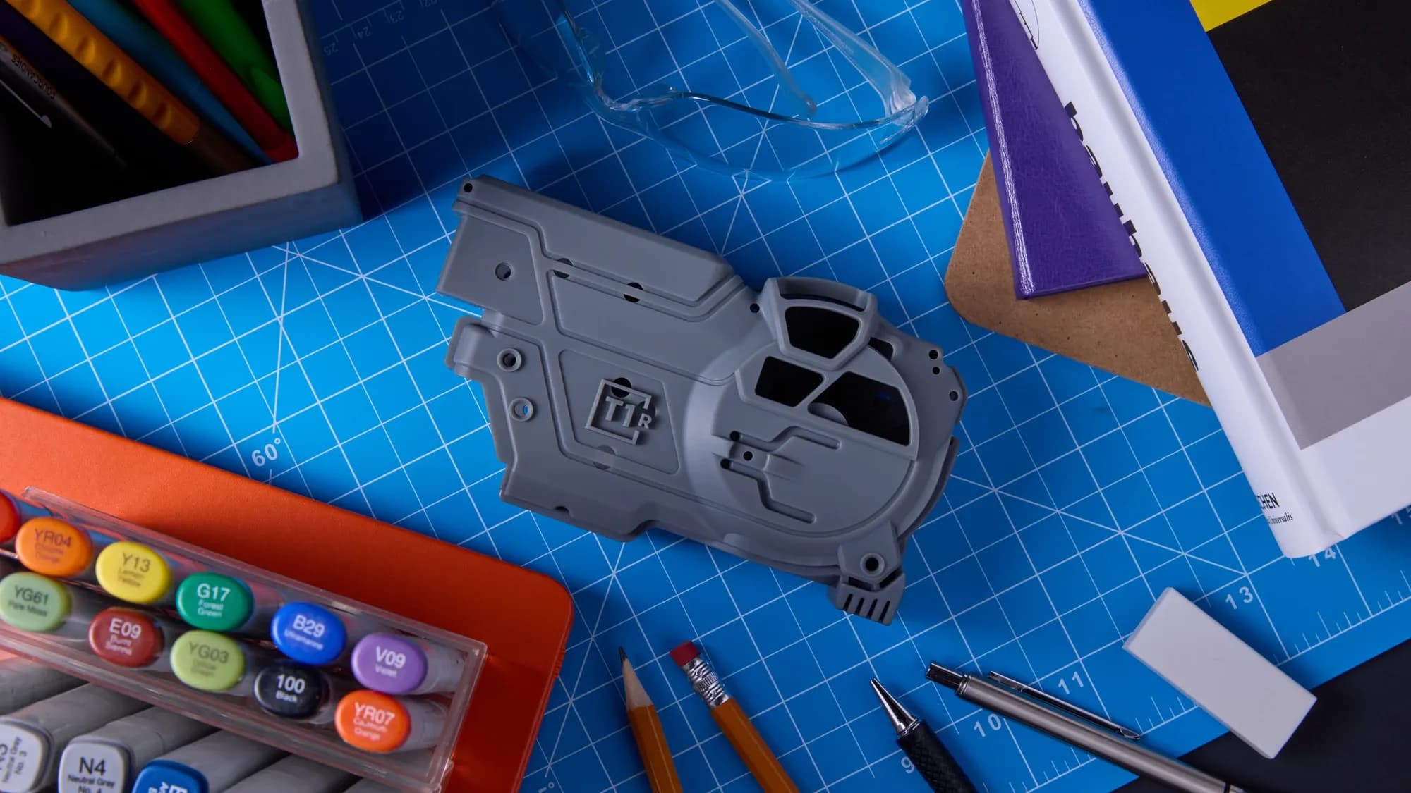 Grey housing prototype on a blue cutting mat beside design tools.